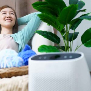 An image of a woman on a couch next to her indoor air quality monitor